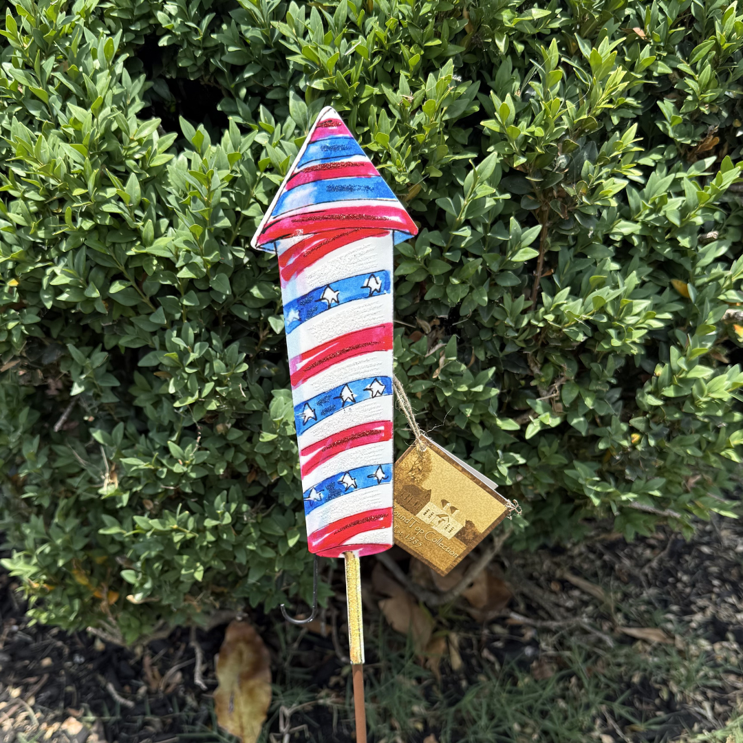 Decorative garden stake with American flag design in front of a green bush